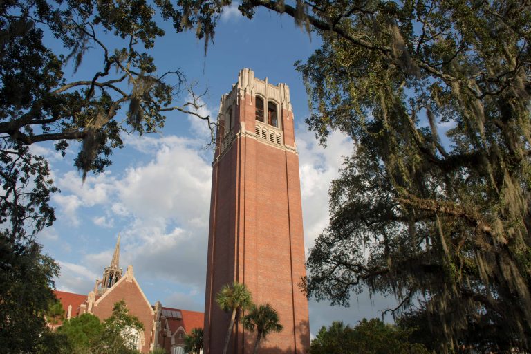 A picturesque brick bell tower with dramatic trees surrounding it and the blue sky in the background
