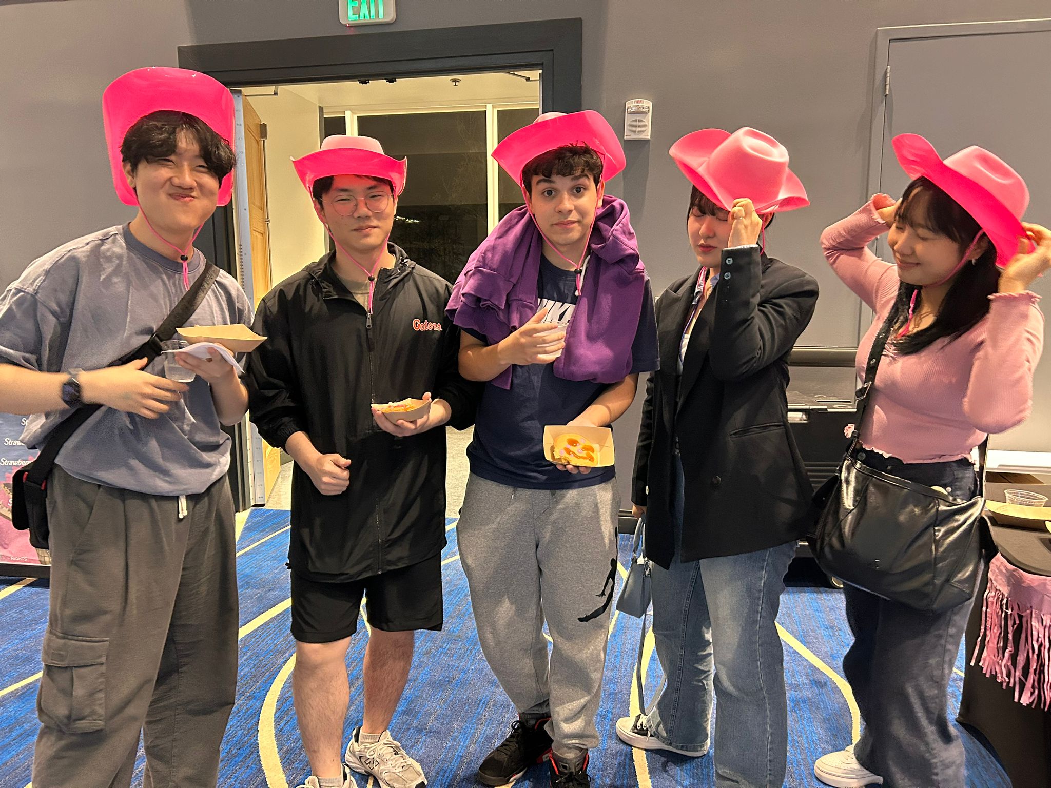 A group of students eating pizza and wearing pink cowboy hats.