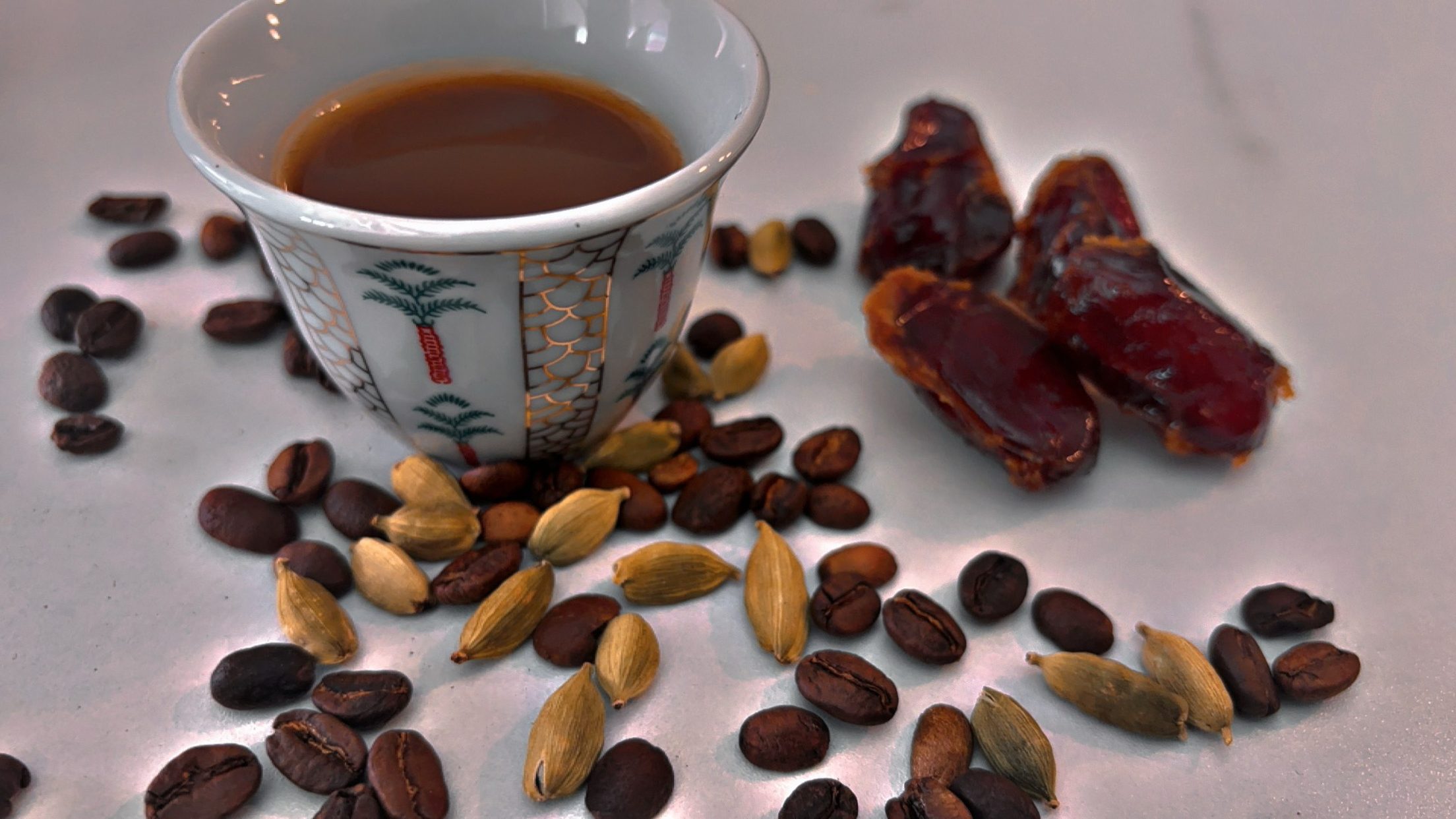 Delicate cup half-filled with Saudi coffee and surrounded by coffee beans, cardamom pods, and dates